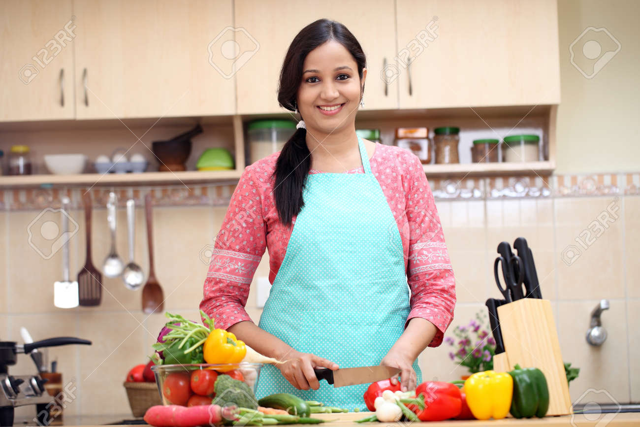 27988789-young-indian-woman-cutting-vegetables-in-kitchen-room